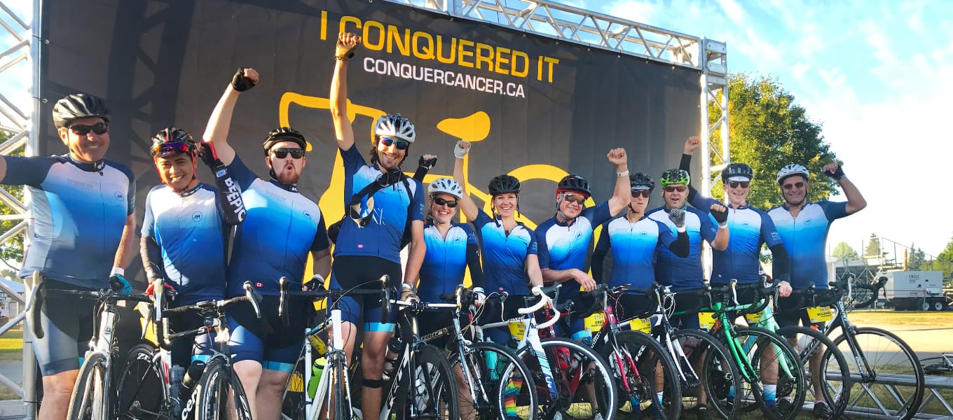 a group of cyclists in blue jerseys on a charity ride to conquer cancer